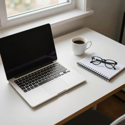 Mesa de trabalho com notebook aberto, caderno, café e óculos.